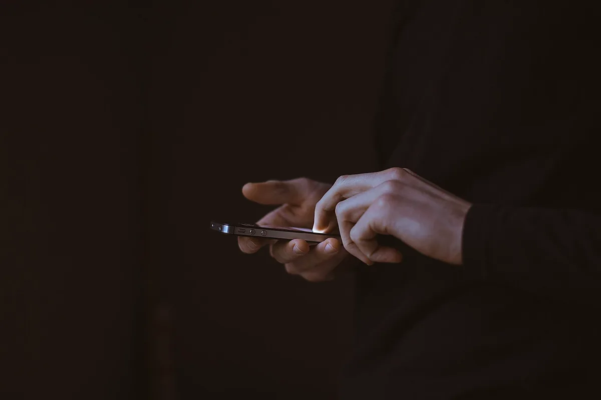 يدان تتصفحان هاتفاً ذكياً في إضاءة خافتة لمتابعة قناة وظائف